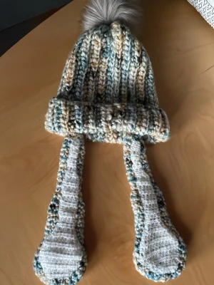 Kanin mössa - Virkad mössa i tjockt myltifärgat garn i blå, beige och turkosa nyanser med lite inslag av svart och gult. Mössan har kaninöron som är ca 35 cm var och mössan har en diameter på 22 cm