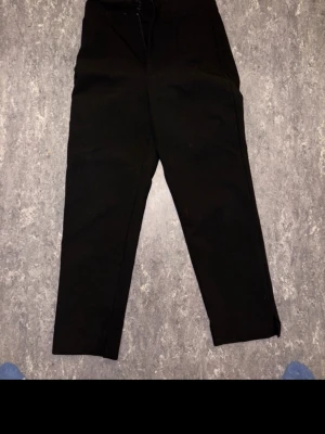 Svarta croppade byxor med dragkedja Högmidja  - Snygga svarta byxor med croppad längd och smalare ben. Byxorna har dragkedja och knapp framtill, vilket ger en clean look. Perfekta att matcha med sneakers eller boots för en chill stil. Materialet känns mjukt och bekvämt mot huden.