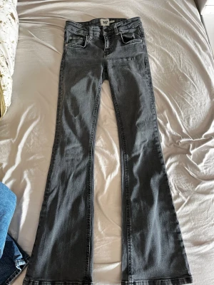 Grå bootcut jeans från 157 XXS - Säljer ett par grå bootcut jeans från 157 i storlek XXS med kort längd. Modellen är lågmidjad och har klassiska fem fickor, bälteshällor och knappstängning. Jeansen är tillverkade i ett mjukt bomullsmaterial med lite stretch för extra komfort.