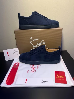 Christian Louboutin Skor - Säljer ett par marinblå sneakers från Christian Louboutin i mjuk mocka med klassisk röd sula och rund tå. Skorna har snörning och beige innersula med guldfärgad logga. Kommer med originalkartong, dustbag och tillbehör. Priset är diskuterbart vid snabb affär