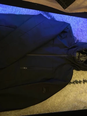 Svart pufferjacka från Jack & Jones - Säljer en svart pufferjacka från Jack & Jones Core med huva och dragkedja framtill. Jackan har två praktiska bröstfickor med dragkedja och en stilren look. Perfekt för kalla dagar och enkel att matcha med olika outfits.