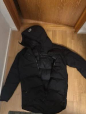 Svart pufferjacka från Sail Racing - Säljer en svart pufferjacka från Sail Racing med huva och dragkedja. Jackan har logga på bröstet och ärmarna samt flera praktiska fickor. Perfekt för kalla dagar och riktigt snygg streetstil. Passar dig som vill ha en varm och stilren jacka.