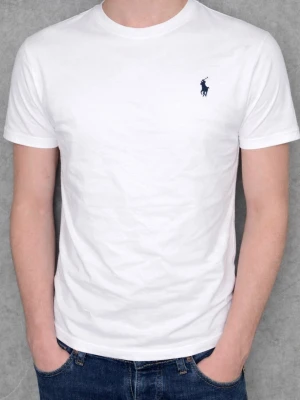 Vit t-shirt från Polo Ralph Lauren - Vit t-shirt från Polo Ralph Lauren med klassisk rund hals och korta ärmar. T-shirten har en snygg marinblå broderad logga på bröstet och är gjord i mjuk bomull som känns skön mot huden. Perfekt för dig som gillar stilrena och tidlösa plagg. Taggar och allt som ingick i köpet skickas med. Krympt lite i storleken så passar S-XS