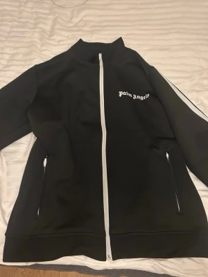 Svart Palm Angels track jacket M - Palm Angels svart track jacket med vita ränder längs ärmarna och vit dragkedja framtill. Jag fick den av min tjej som julklapp men den passar inte mig jag köpte den för 1500kr 