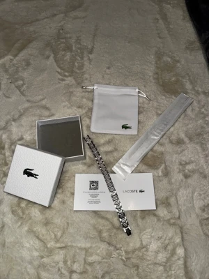 Silver Lacoste Armband Metropole - Helt ny Silver Lacoste Armband med tillbehör:  Låda, dammpåse, autencitet dokumenter, armbandshållare + plastskydd, mobilskan. Fräsch och snygg armband och perfekt för present 🎁 ete