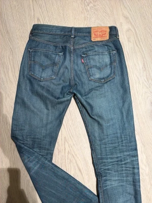 Levi's 501 blå jeans straight fit - Vintage Klassiska blå Levi's 501 jeans med raka ben och femficksmodell. Jeansen har en snygg tvättad look, orange sömmar och den ikoniska läderpatchen bak i midjan. Tillverkade i slitstarkt denim med knappgylf och normal passform.