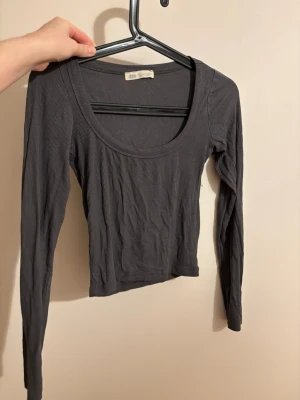Mörkgrå ribbad långärmad topp - Säljer en mörkgrå ribbad långärmad topp från Sthlm Atelier. Toppen har en djup rundad halsringning och är croppad i modellen. Perfekt att styla med jeans eller kjol för en chill look.