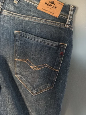 Replay Jakors med slitningar - Säljer ett par snygga Replay jeans i klassisk blå färg med coola slitningar . Jeansen har raka ben, fem fickor och kontrastsömmar. Materialet är denim och passformen är normal (ganska rak). Perfekt för dig som gillar en avslappnad streetstil. 