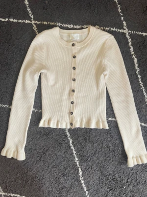Beige ribbad kofta med volangkantp - Snygg beige ribbad kofta med volanger ifrån hm! Koftan är knappt använd och den är super fin och passar perfekt till en vardags outfit. Original priset är 299kr och eftersom den knappt är använd så säljer jag den för 149 kr! (Går dock att diskutera)💕💕💕