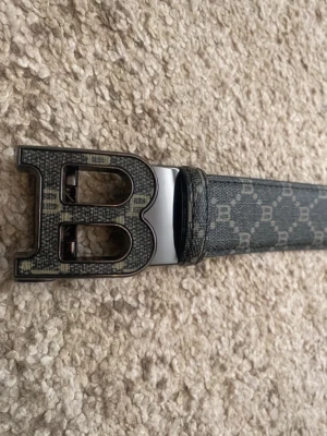 Bälte - Helt nya/oanvända stilrena bälten säljes med rutiga svart/grå formade rutor och med ett B-spänne Finns i 90 cm, 100 cm, 110 cm, 120 cm… osv Kopi men högkvalitativa och stilrena som lyfter hela outfiten.