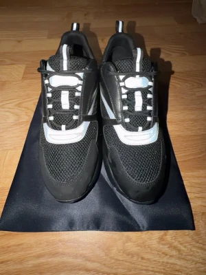 Svarta Dior sneakers med vit detalj - Säljer ett par chunky Dior sneakers i svart med vita och silverfärgade detaljer. Skorna har mesh och skinnmaterial, snörning och plattformssula. Snygg design med rund tå och coola kontraster. Perfekta för dig som gillar statement-sneakers.