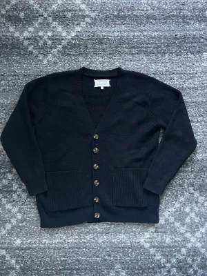 Svart cardigan från Maison Margiela - Säljer en svart cardigan från Maison Margiela med ribbstickad struktur. Långärmad och tillverkad i mjukt stickat material som känns riktigt skönt mot huden.
