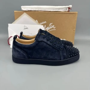 Mörkblå sneakers från Christian Louboutin - Snygga mörkblå sneakers från Christian Louboutin i mocka med ikoniska röda sulor och svarta nitar på tån. Skorna har rund tå, snörning och en platt sula. Perfekt för dig som vill sticka ut med exklusiv design och coola detaljer.
