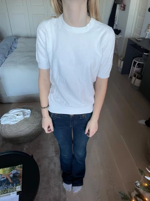 Vit kortärmad stickadtopp från Zara - Säljer en vit, enkel och stilren topp från Zara i storlek S. Toppen har rund halsringning och korta ärmar med ribbade muddar. Materialet är mjukt och känns som bomull, perfekt för en clean look. Passformen är normal och toppen är enfärgad utan mönster.