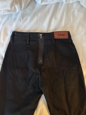 Svarta skinny jeans från Acne studios  - Svarta jeans från Acne studios med klassisk skinny passform och hög midja. Snyggt Acne-läderpatch framtill och dragkedja baktill. Jeansen har bälteshällor och är tillverkade i ett mjukt bomullsmaterial med lite stretch för extra komfort. Storlek 27/32. (Första bilden är där bak)