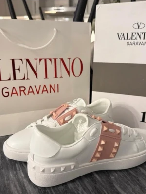 Valentino Rockstud sneakers vit/rosa - Säljer ett par Valentino Rockstud sneakers i vitt skinn med ljusrosa panel och ikoniska pyramidnitar. Skorna har rund tå, platt sula och snörning framtill. Märkeslogga på plösen och detaljerade nitar längs sidan och bak på sulan. Perfekt för dig som gillar statement-detaljer. Priset kan diskuteras☺️