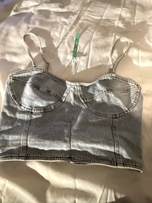  Jeans korsett-topp👖🦋 - Säljer en ljusblå korsett-topp från Gina Tricots Perfect Jeans i jeansmaterial. Toppen har smala justerbara axelband, markerade kupor och elastisk rygg för skön passform. Snygga sömmar framtill och croppad modell som ger en cool vibe. Perfekt till jeans eller kjol!🦋✨