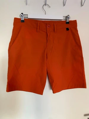 Orange golfshorts från Peak Performance - Snygga orange golfshorts från Peak Performance i modellen MAXWELLSH. Klassisk design med raka ben, bälteshällor, sidofickor och två bakfickor. Tillverkade i ett mjukt bomullstyg som passar perfekt till golfsäsongen. Stängs med knapp och dragkedja framtill. Passar väldigt bra med den vita Lacoste Pikén i en annan annons jag har. 
