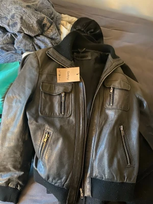 svart/grå skinnjacka - snygg svart/grå jacka i skinn med ribbade muddar och krage. jackan har flera fickor med dragkedjor både fram och på bröstet, samt en kraftig dragkedja i mitten. perfekt för dig som gillar en cool och klassisk stil. köptes på sellpy för 500kr och har ej kommit till användning. står storlek L men passar mer som M