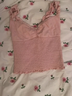 Rosa smockad linnetopp från Kimchi Blue - Supersöt ljusrosa linnetopp från Kimchi Blue eller Urban outfitters  i storlek M, men sitter som XS. Toppen har smockad nederdel, spetsdetaljer vid axelbanden och en omlottliknande byst. Aldrig använd