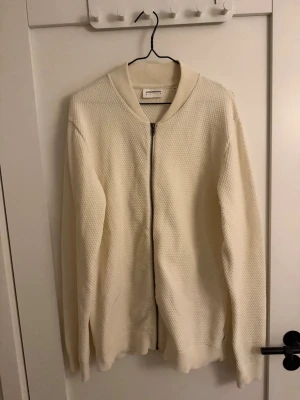 Vit kofta från Lindbergh White XL - Säljer en stilren vit kofta från Lindbergh White i storlek XL. Koftan har ett diskret strukturerat mönster, ribbad krage och muddar samt dragkedja framtill. Perfekt för lager-på-lager och enkel att matcha med jeans eller chinos.