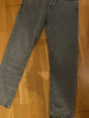 Grå Tapered Mike jeans Jack & Jones - Säljer ett par grå tvättade jeans från Jack & Jones, modell Tapered Mike. Jeansen har fem fickor, bälteshällor och klassisk knappgylf. Passformen är tapered med något smalare ben och materialet är robust denim.