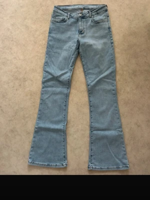 Ljusblå bootcut jeans low flare - Säljer ett par ljusblå jeans med bootcut och låg midja. Modellen heter low flare och har klassisk femficksdesign, dragkedja och knapp framtill. Materialet är jeans och passformen är loose med utsvängda ben. Perfekt för dig som gillar retrovibbar och bekväm stil.