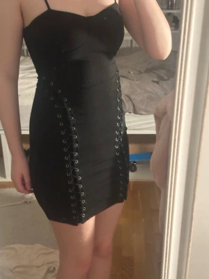 Svart kort klänning med snörning - Säljer en svart, tight kortklänning med smala axelband och cool snörningsdetalj längs sidorna. Klänningen har en figurnära passform och ger en edgy vibe. Perfekt för dig som gillar att sticka ut med detaljer. Den är tyvärr för liten för mig😢😢