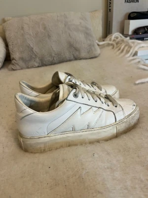Vita sneakers från Zadig & Voltaire - Ge gärna prisförslag💖Säljer ett par vita sneakers från Zadig & Voltaire med coolt blixtdetalj på sidan och logga på hälen. Skorna har snörning, rund tå och platt sula med mönstrad undersida där märket står. Skorna är inte tvättade därför är de smutsiga. Men det går att få bort❗️