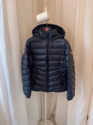 Mörkblå Colmar dunjacka med huva - Snygg mörkblå dunjacka från Colmar med huva och dragkedja framtill. Jackan har ett quiltat mönster och två sidofickor. Ny pris ligger på 3950 kr. Perfekt för kalla dagar i vardagen eller vid finare tillfällen. Jackan har en clean, sportig look som funkar till många stilar. Jackan är använd max fem gånger och är som ny. Bara höra av sig vid funderingar, pris går att diskutera.