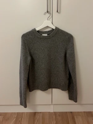 Grå stickad tröja från H&M - Mysig grå stickad tröja från H&M i storlek S. Tröjan har rund hals, ribbade muddar vid ärmslut och nederkant samt långärmad passform. Perfekt för kyliga dagar och enkel att matcha med jeans eller kjol.