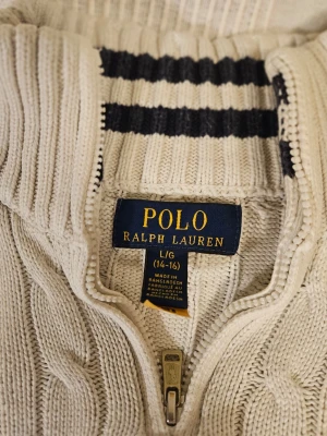 Polo Ralph Lauren Tröja Vit Bomull Pojke 146 till 52 - Polo Ralph Lauren tröja för pojkar i storlek 146. Tillverkad i bomull med vit färg. Tröjan har en kabelstickad design och en halv dragkedja vid halsen. Köpte för 1800.