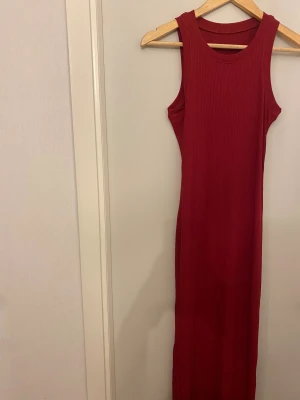 Röd ribbad långklänning - Snygg röd långklänning med ribbad struktur och ärmlös design. Klänningen har rund halsringning och sitter figurnära längs kroppen. Perfekt för dig som gillar enkel men stilren look och vill sticka ut med färg.