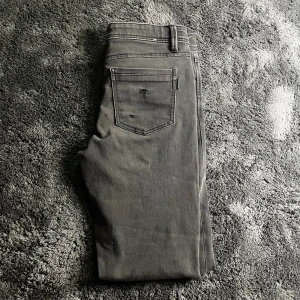 Grå slim fit jeans med slitningar - Snygga grå jeans i skinny fit med slitna detaljer på fram- och bakfickor. Klassisk femficksmodell med dragkedja och knapp framtill. Jeansen har en slim passform och är tillverkade i stretchigt denimtyg för extra komfort.