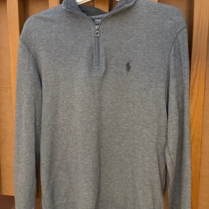 Grå half zip tröja från Polo Ralph Lauren - Tja! Säljer en fin grå half zip från polo ralph lauren då den är för stor för mig. Jag är 170 och skulle säga att tröjan passar dig som är 175-180. Tröjan är riktigt snygg och passar de flesta stilar och människor. Köp den så piffar du till din garderob direkt. Inga defekter. Nypris: 2100kr. Ha det fint!
