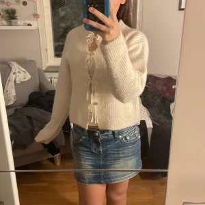 Vit stickad bolerotopp med rosetter - Superfin vit bolerotopp i stickat material med fyra söta rosetter framtill. Modellen är croppad och har lång ärm samt rund halsringning. Perfekt för dig som gillar gulliga detaljer och vill ha en mysig men stylish look.