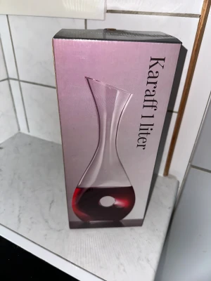 Karaff 1 liter - Elegant karaff i glas med 1 liters kapacitet, perfekt för servering av vin eller vatten. Modern design med rundad botten och hål för enkel hantering. Produkten ser oanvänd ut och levereras i originalförpackning. Inga synliga defekter eller slitage. Perfekt för att ge till gåva 🎁 överraska någon du håller kär ❤️