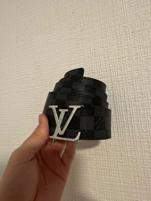 Svart rutigt bälte - Svart rutigt bälte med silver badge  i storlek 110