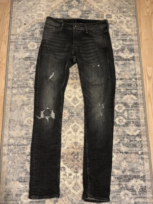 Jack and Jones jeans slitningar - Säljer ett par svarta jeans från Jack & Jones med coola slitningar och distressed detaljer på benen. Sitter riktigt bra på benen, slim fit. Köpta för några månader sedan men aldrig använt. Nytt pris 900kr mitt pris 500kr. 