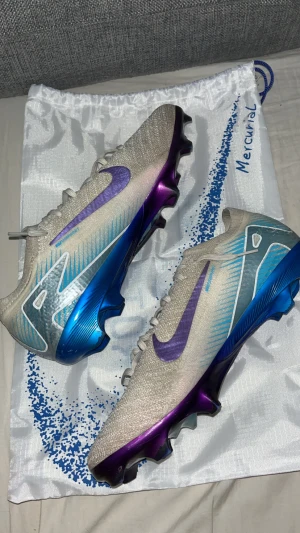 Nike Mercurial fotbollsskor blå/lila - Säljer ett par Nike Mercurial fotbollsskor i en futuristisk design med silverfärgad ovandel, lila Swoosh och blå detaljer. Skorna har snörning och en cool, skimrande blå och lila sula. Perfekta för dig som vill sticka ut på planen! Obs dom är kopior