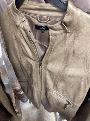 Beige skinnjacka från Isolde - Snygg beige skinnjacka från Isolde med stilrena sömmar och två dragkedjefickor framtill. Jackan har en klassisk krage och dragkedja hela vägen upp. Perfekt för dig som gillar en clean och cool look.