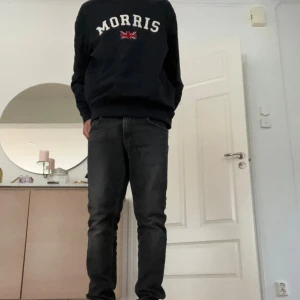 Svart sweatshirt från Morris - Svart sweatshirt från Morris med broderad logga och brittisk flagga på bröstet. Klassisk rund halsringning och långa ärmar. Tillverkad i mjuk bomull för en skön och avslappnad stil.