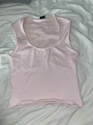Ljusrosa linnetopp från Gina Tricot - Supersöt ljusrosa linnetopp från Gina Tricot i storlek L. Toppen är ärmlös med rundad halsringning och har en liten rosett framtill som detalj. Materialet är mjukt och ribbat.