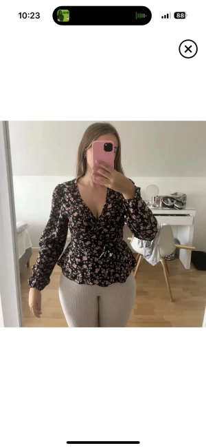 Svart blommig omlottblus med knyt - Säljer en svart blommig omlottblus med rosa och ljusa blommor. Blusen har v-ringning, långa ärmar med lätt puff och knyt i midjan. Materialet känns lätt och flowy, perfekt för dig som gillar romantiska detaljer och markerad midja. Knappt använd helt felfri.