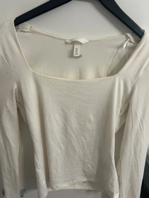 Vit långärmad topp från H&M - Säljer en stilren vit långärmad topp från H&M med fyrkantig urringning. Toppen är i mjuk bomull och har en clean, enkel look som är lätt att matcha. Perfekt för dig som gillar minimalistisk stil och vill ha en basic i garderoben.