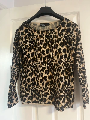 Leopardmönstrad stickad tröja - Snygg stickad tröja i storlek XS och passar S med leopardmönster i svart och brunt på beige botten. Rund halsringning och långa ärmar. Perfekt för dig som vill sticka ut med ett djuriskt print och samtidigt hålla det bekvämt.