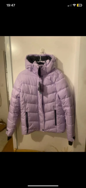 Ljuslila pufferjacka från McKinley - Säljer en ljuslila pufferjacka från McKinley med huva och svarta detaljer vid dragkedjorna. Jackan är quiltad och har långa ärmar med muddar. Perfekt för kalla dagar och har en snygg, modern look. Färg: light purple. Finns att hämta direkt!