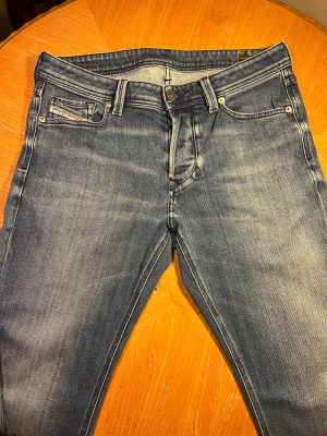 Diesel Larkee blå tapered jeans - Snygga blå jeans från Diesel, modell Larkee, med tapered fit och klassisk femficksdesign. Jeansen har en cool tvätt med ljusa partier och tydliga sömmar, samt Diesel-logga på bakfickan och läderpatch i midjan. Perfekt för dig som gillar stilrena och bekväma jeans.