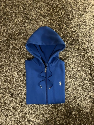 Blå hoodie från Polo Ralph Lauren - Supertrendiga tröjan från Ralph lauren i varmt och tjockt material som är bra till vintern, använd ca 4-5 gånger så i väldigt fint skick och sitter ganska slim i storleken passar typ xs/s, Pris kan diskuteras vid snabbt köp