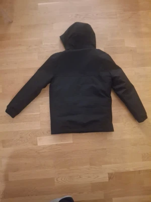 Svart vindjacka från Polo Ralph Lauren - Svart vinterjacka från Polo Ralph Lauren med huva och två snedställda fickor med dragkedja. Jackan har det klassiska Polo-logot broderat på bröstet och elastiska muddar vid ärmsluten. Perfekt för dig som gillar stilren och sportig look.